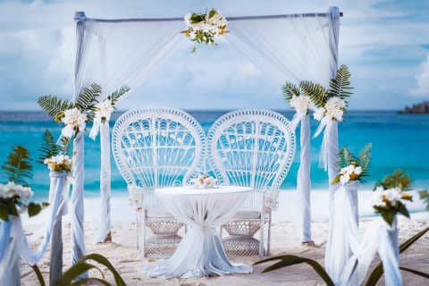 Beach wedding arch gazebo ceremonial decorated with white flowers on a tropical grand anse sand beach. Outdoor beach wedding setup. La Digue, Seychelles.